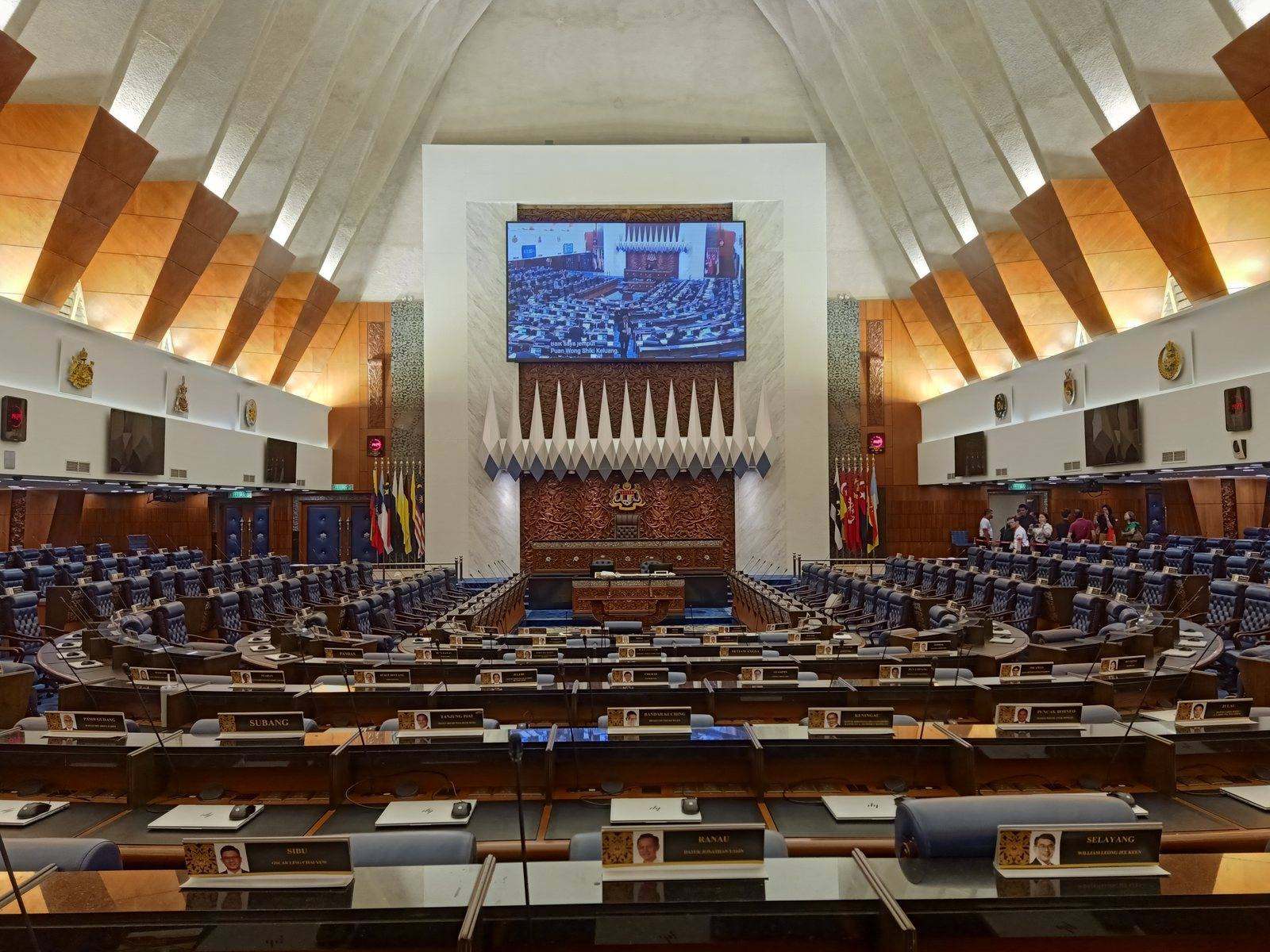 The interior of the Dewan Rakyat, the lower house of the Parliament of Malaysia, showing the tiered seating and the Speaker's chair beneath a large screen