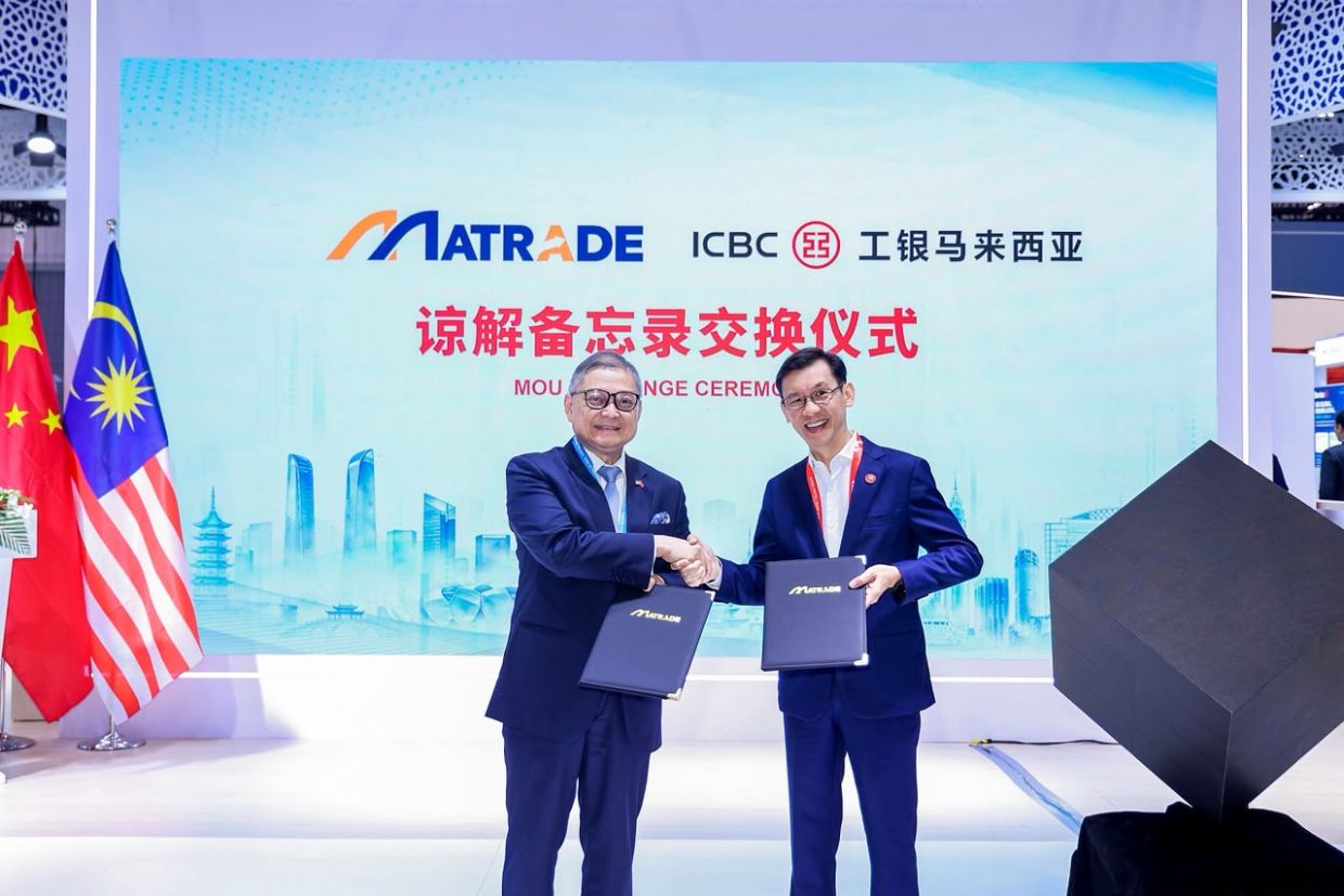 Two officials exchange memorandum of understanding folders at the Malaysia Pavilion during the Global Digital Trade Expo in Hangzhou, with the MATRADE and ICBC Malaysia marks and the Malaysian and Chinese flags behind them