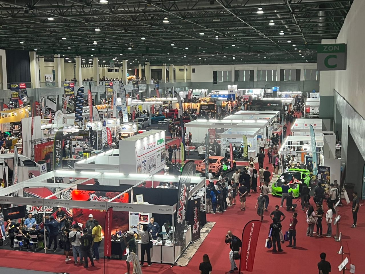 Wide view of a busy MIAPEX show floor with exhibitor booths, red carpet aisles and crowds at MIECC