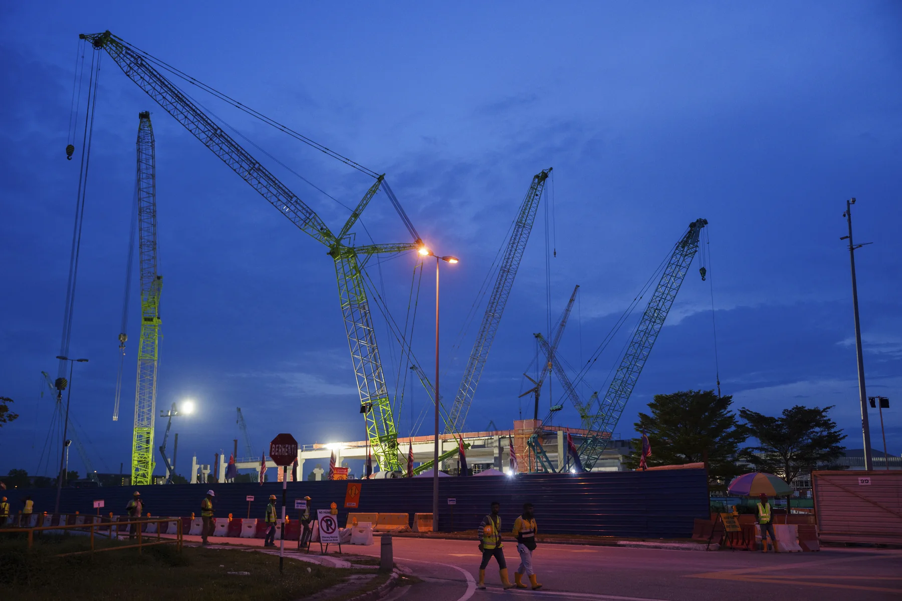 Construction workers walk outside a data centre building under construction in Johor Bahru at dusk, with tower cranes behind them